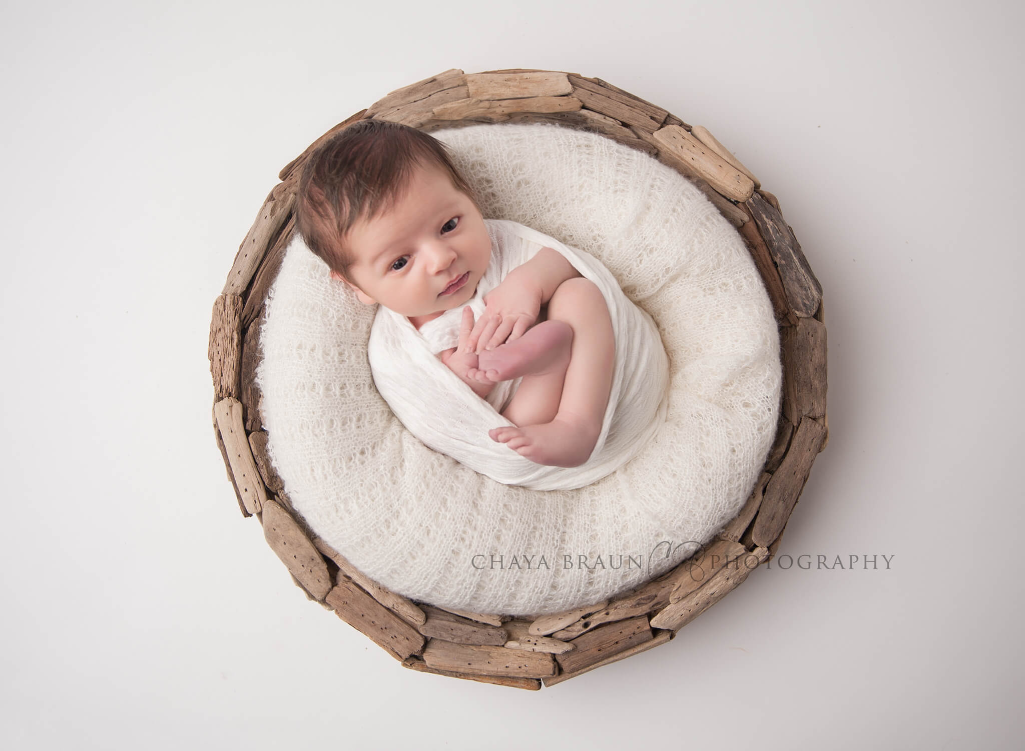 awake newborn baby in driftwood basket