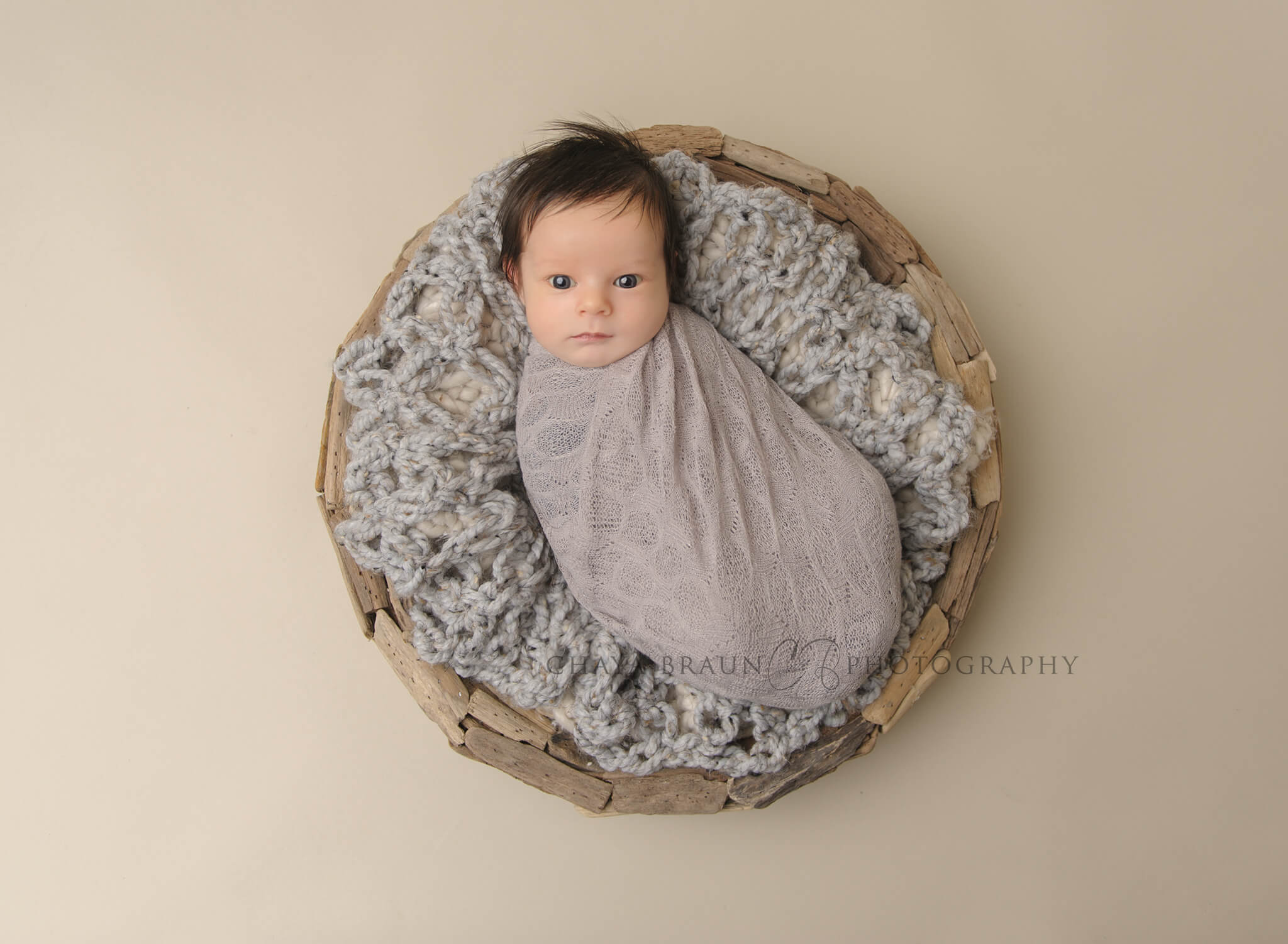 awake newborn baby boy in gray driftwood basket